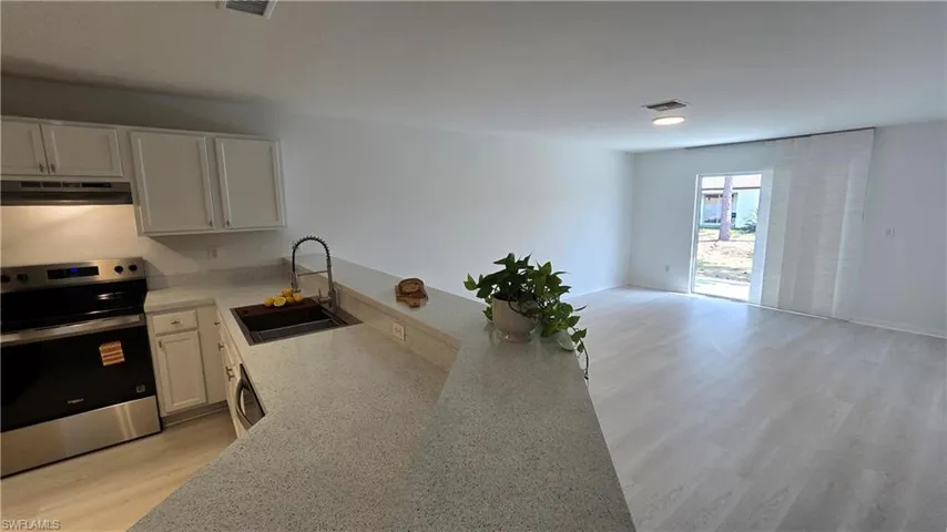 Kitchen with stainless steel range with electric stovetop, light wood-style floors, white cabinets, light stone countertops, and open floor plan