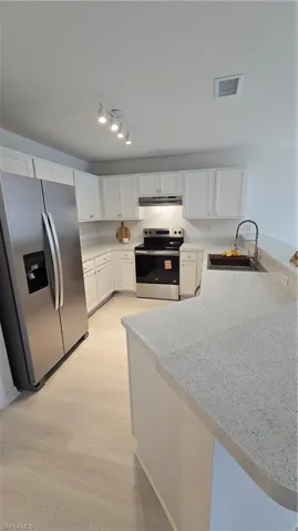 Kitchen featuring refrigerator, a peninsula, white cabinets, electric range, and rail lighting