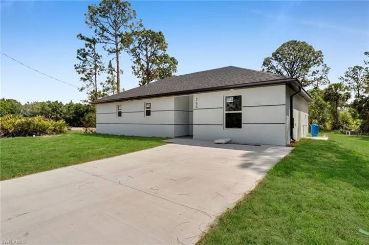 View of front of property with a patio, a shingled roof, a front lawn, and stucco siding