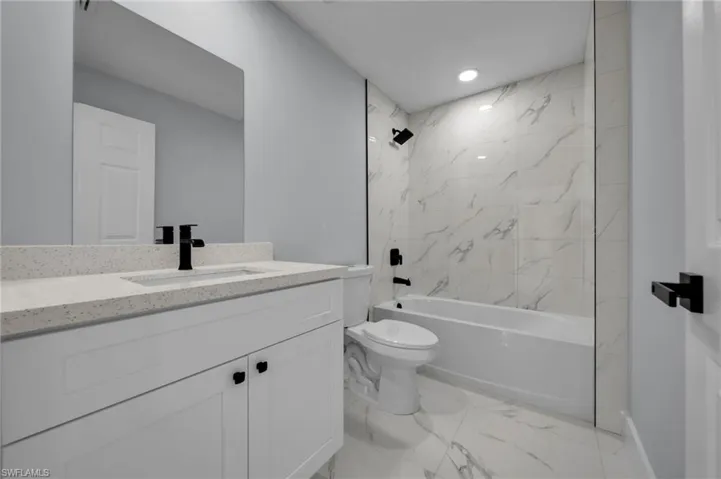 Full bathroom with vanity, marble finish floor, toilet, baseboards, and shower / bath combination