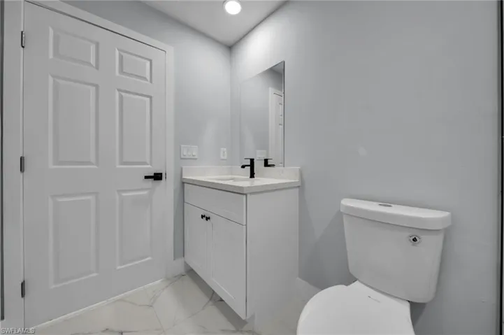 Bathroom with vanity, baseboards, toilet, and marble finish floor