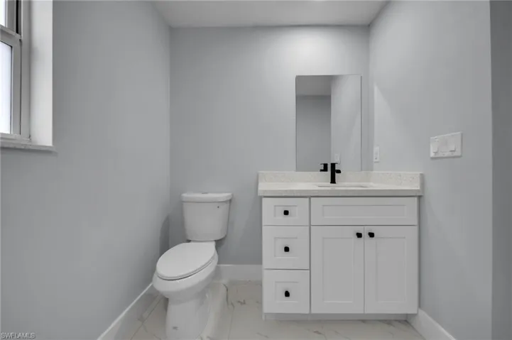 Half bath with toilet, baseboards, marble finish floor, and vanity