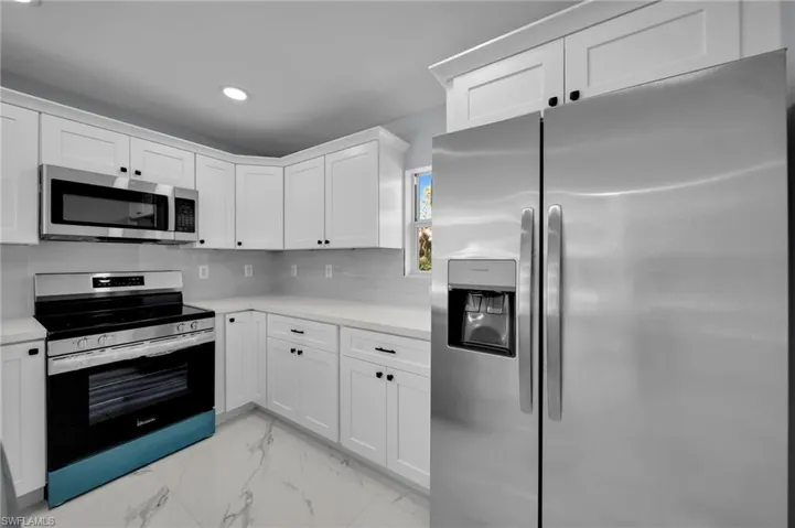 Kitchen featuring appliances with stainless steel finishes, tasteful backsplash, light countertops, marble finish floor, and white cabinetry