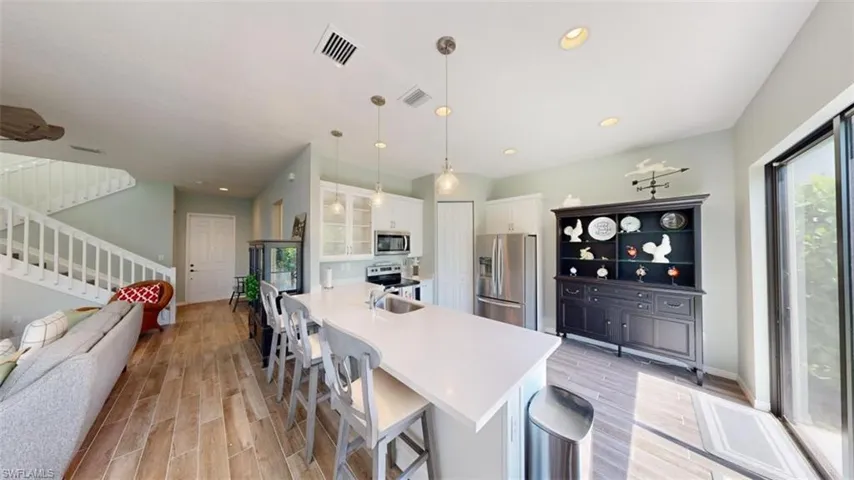 Kitchen featuring light hardwood / wood-style floors, decorative light fixtures, a breakfast bar, white cabinetry, and appliances with stainless steel finishes