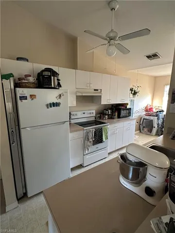 Kitchen featuring white appliances, white cabinets, ceiling fan, vaulted ceiling, and light countertops