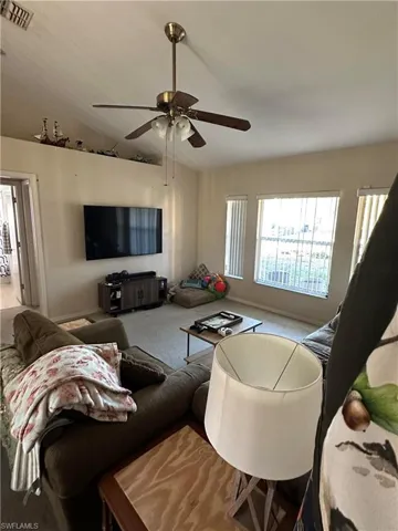 Living room with vaulted ceiling, a ceiling fan, and carpet flooring
