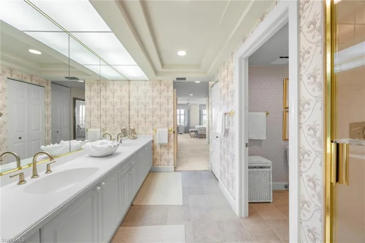 Ensuite bathroom featuring a raised ceiling, double vanity, recessed lighting, wallpapered walls, and light tile patterned floors