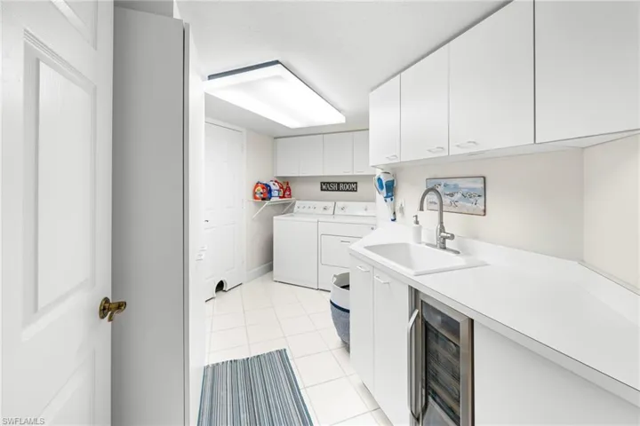 Laundry area featuring wine cooler, light tile patterned floors, washer and dryer, and cabinet space