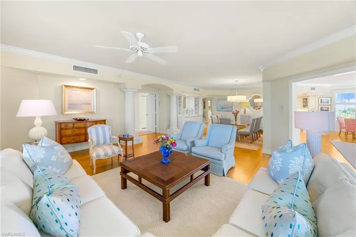 Living area with wood finished floors, decorative columns, ornamental molding, arched walkways, and ceiling fan
