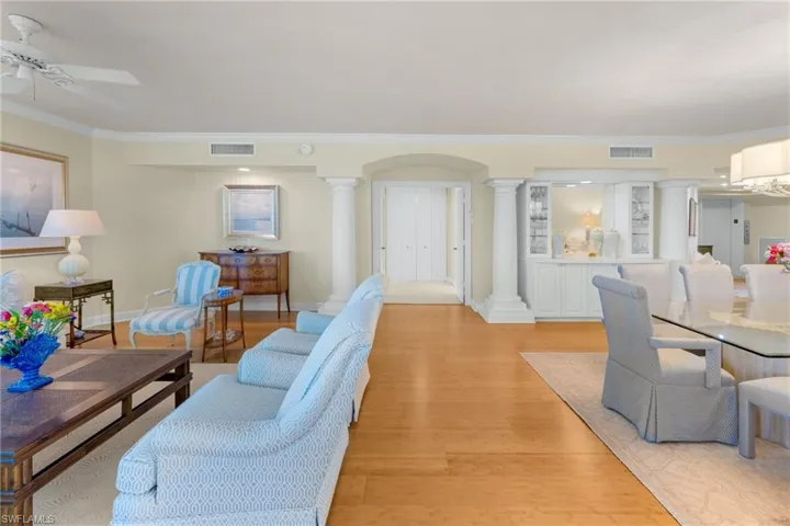 Living area featuring light wood finished floors, crown molding, ornate columns, a ceiling fan, and arched walkways