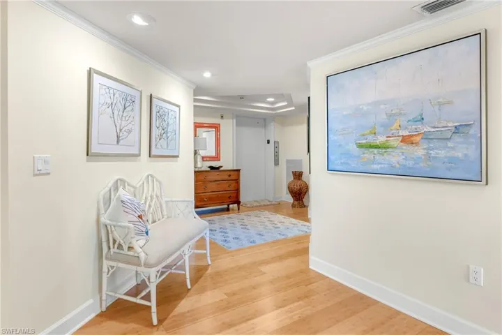 Hall with ornamental molding, light wood-type flooring, recessed lighting, elevator, and a raised ceiling