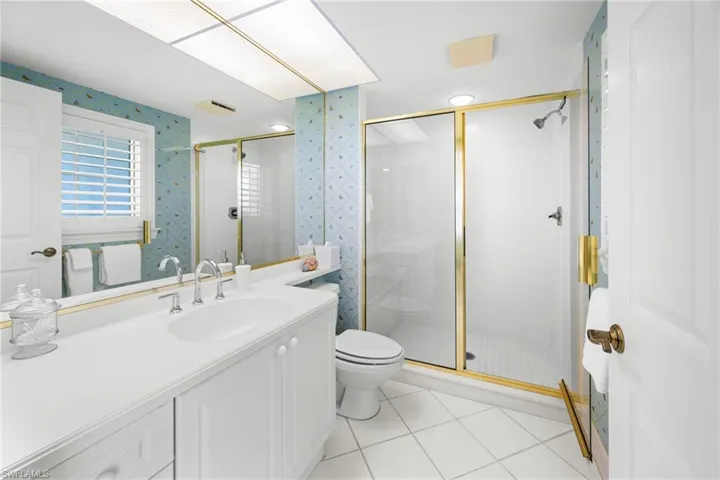 Bathroom featuring a stall shower, vanity, light tile patterned floors, and wallpapered walls
