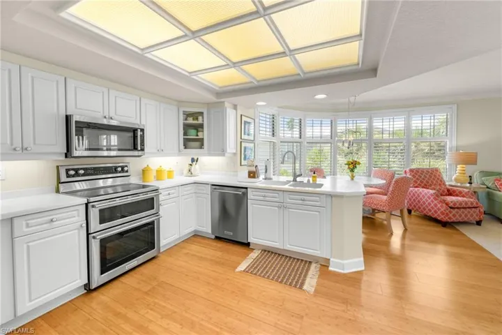 Kitchen with a peninsula, stainless steel appliances, white cabinetry, light wood finished floors, and a tray ceiling