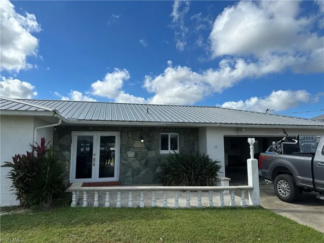 View of side of home featuring a metal roof, driveway, french doors, stone siding, and a garage