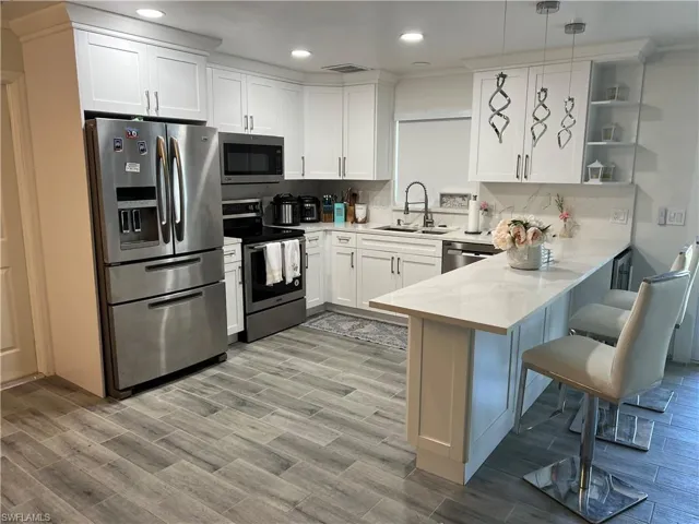 Kitchen featuring stainless steel appliances, white cabinetry, wood finish floors, and a peninsula