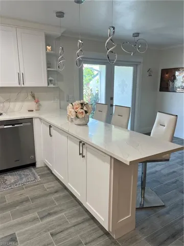 Kitchen with open shelves, decorative light fixtures, dishwashing machine, light stone counters, and a peninsula