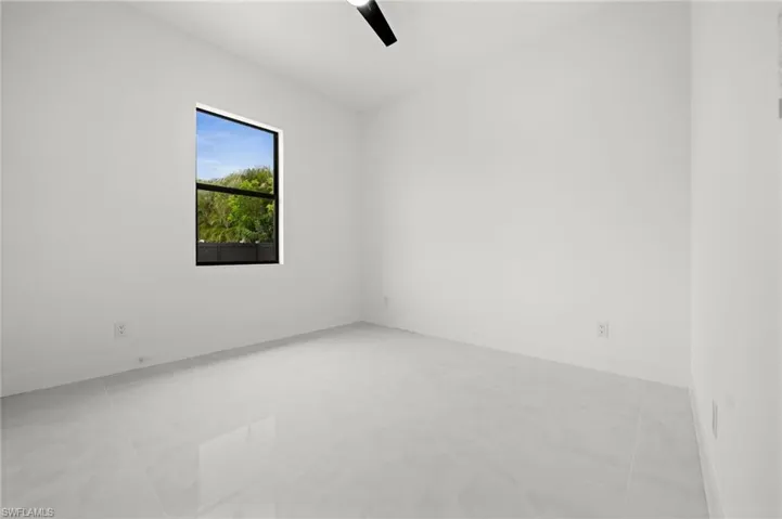 Spacious room featuring light-toned tile flooring, a large window with exterior foliage, a ceiling fan, and white baseboards