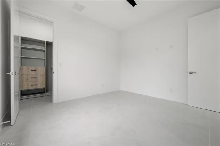Bright room with light-toned tiled flooring, featuring a built-in closet system with shelving and wood-finish drawers