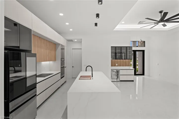 Modern kitchen featuring an expansive island with a waterfall edge, integrated appliances, recessed lighting, and a contemporary ceiling fan