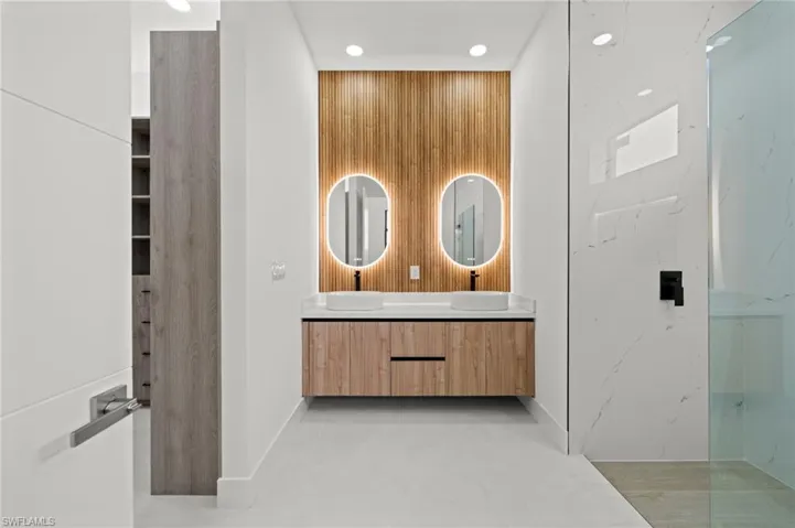 Modern bathroom featuring a dual vanity with vessel sinks, back-lit oval mirrors, and a wood-finish slatted accent wall
