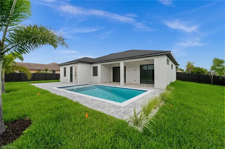 Contemporary single-story home featuring a rectangular swimming pool, paver patio, lush green lawn, private fencing, and a covered patio area
