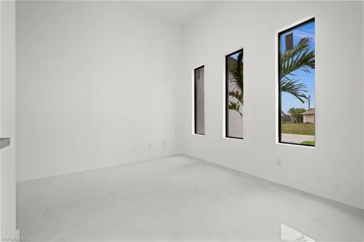 Bright interior space featuring three vertical windows with black frames, white walls, light-toned tile flooring, and white baseboards