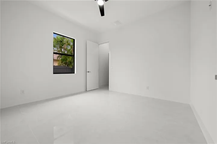Spacious room featuring light-toned tile flooring, neutral wall finishes, a ceiling fan, and a single window with dark framing