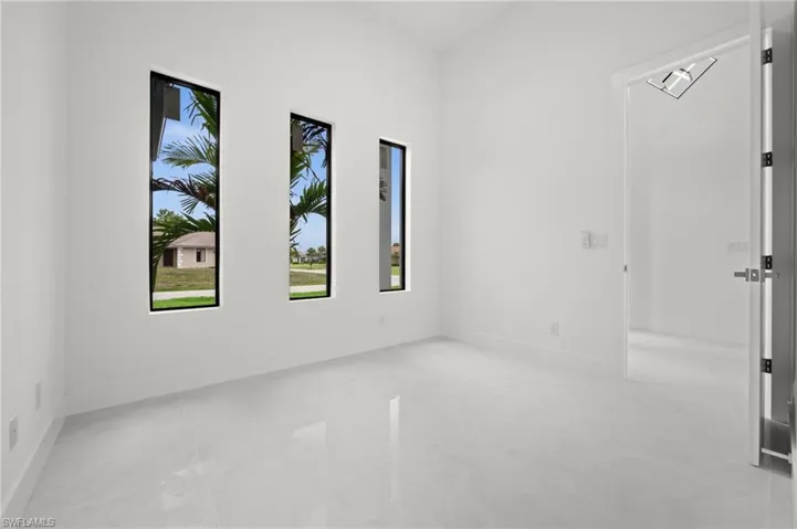 Light-filled room featuring three vertical windows with black frames, white walls, white baseboards, and large format polished tile flooring