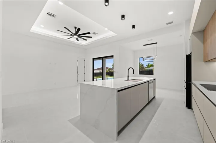 Open-concept living space with large format tile flooring and a tray ceiling featuring recessed lighting and a ceiling fan