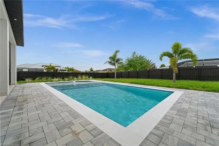 Rectangular in-ground swimming pool with a white coping, surrounded by a grey paver patio