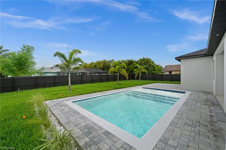 Backyard oasis featuring a rectangular swimming pool with integrated steps, surrounding paver decking, and a privacy fence