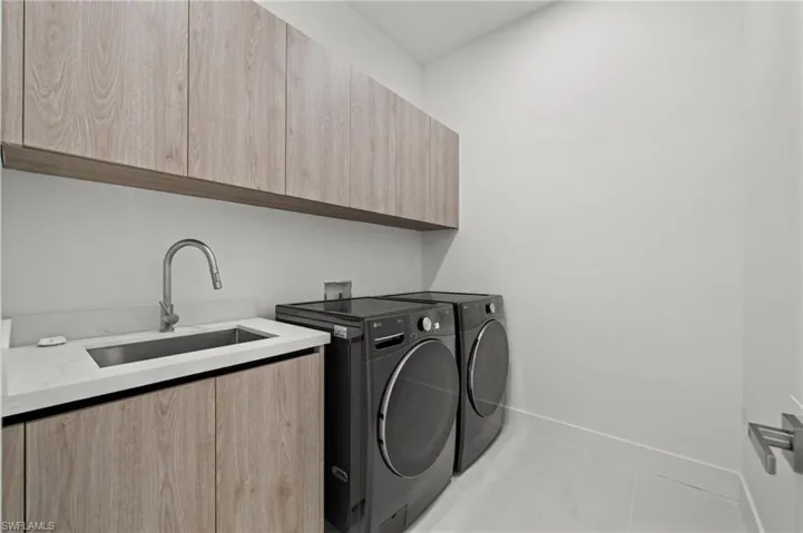 Laundry area featuring a built-in stainless steel sink with a gooseneck faucet, white countertop, and wood-finish cabinetry