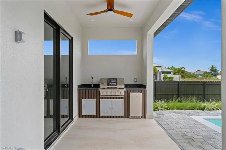 Covered outdoor kitchen featuring a built-in grill, sink, and under-counter refrigerator