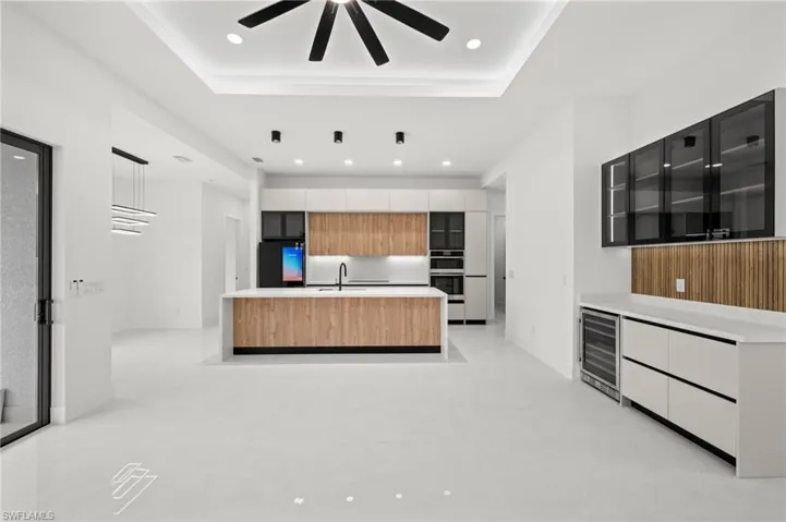 Contemporary kitchen and bar area featuring white tile flooring, wood-finish cabinetry, a central island with integrated sink, built-in appliances, and recessed lighting