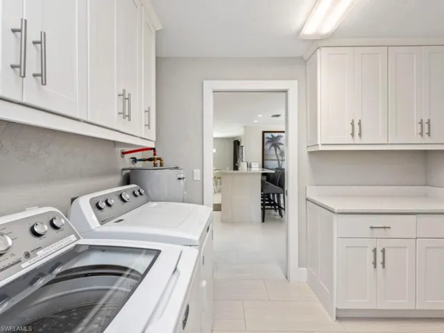 Laundry area with cabinet space, washing machine and dryer, water heater, and light tile patterned flooring