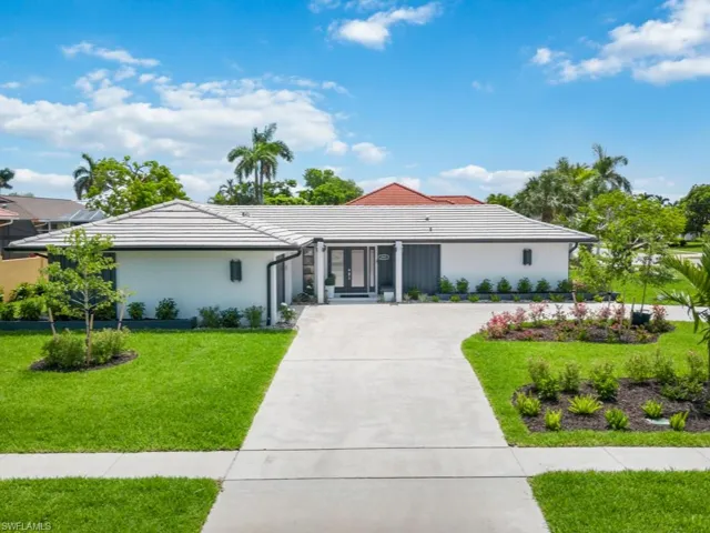 View of front of property with concrete driveway, stucco siding, a front lawn, and a tile roof