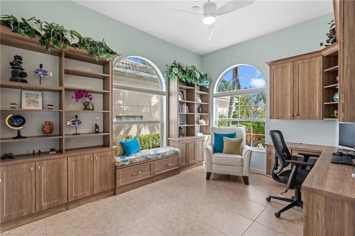 Home office with a ceiling fan and convenient, custom, built-in desk, window seat, and storage shelves.