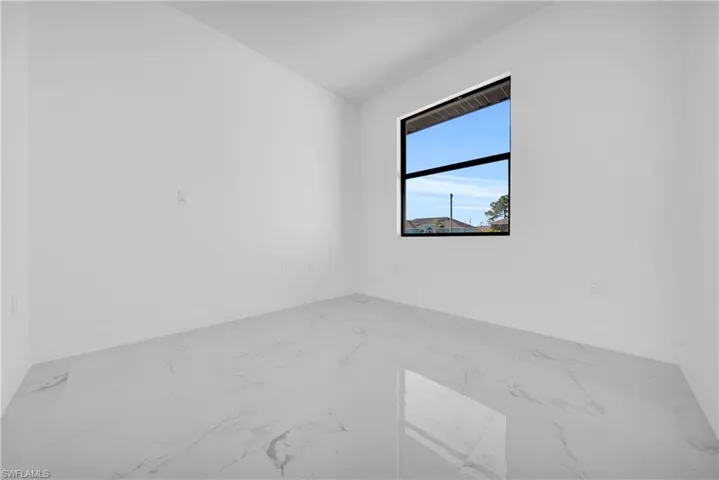 Unfurnished room featuring light marble finish floors and lofted ceiling