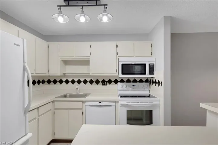 Kitchen with white appliances, light countertops, white cabinets, and tasteful backsplash