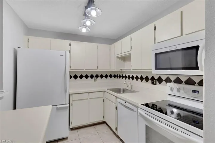 Kitchen featuring white appliances, light countertops, light tile patterned floors, white cabinetry, and a textured ceiling