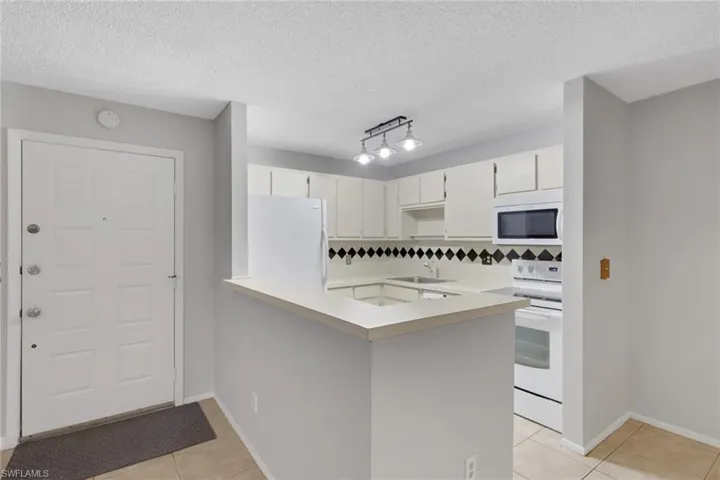 Kitchen with light countertops, white appliances, light tile patterned floors, a textured ceiling, and white cabinets