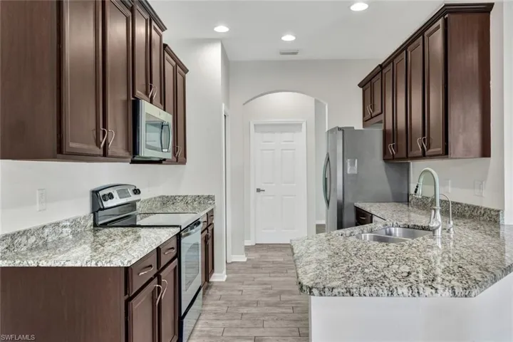 Kitchen with light stone countertops, sink, dark brown cabinets, appliances with stainless steel finishes, and light wood-type flooring