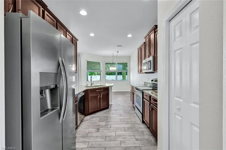 Kitchen with pendant lighting, sink, light hardwood / wood-style flooring, light stone countertops, and appliances with stainless steel finishes