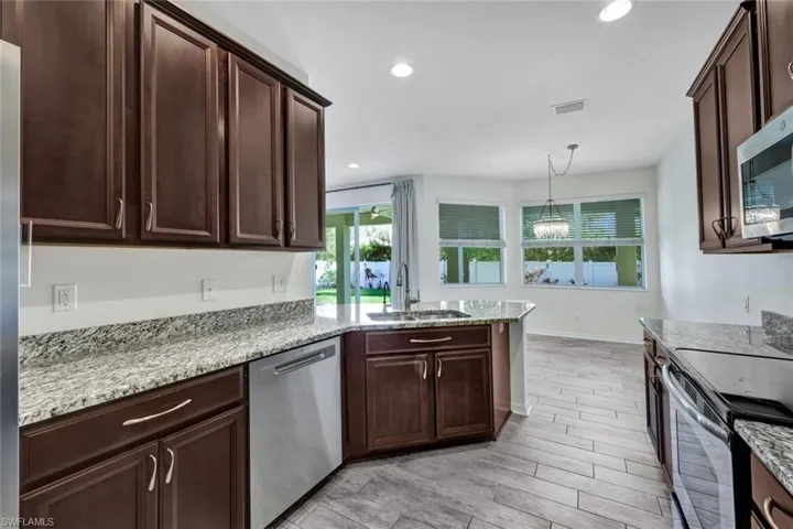 Kitchen featuring sink, hanging light fixtures, light hardwood / wood-style floors, light stone counters, and stainless steel appliances