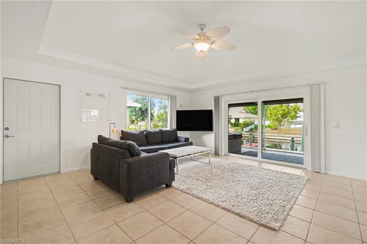 Living room featuring a tray ceiling, a ceiling fan, and light tile patterned floors