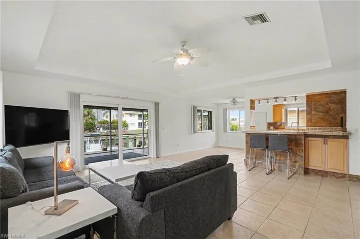 Living room with a tray ceiling, light tile patterned floors, plenty of natural light, ceiling fan, and track lighting