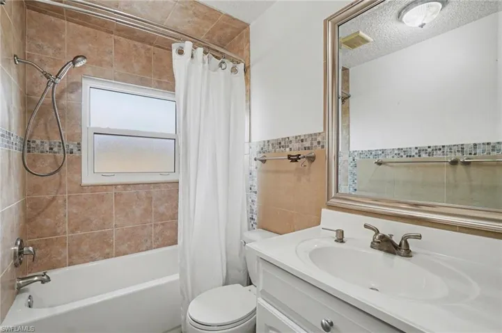 Full bath featuring vanity, shower / tub combo with curtain, tile walls, and a textured ceiling
