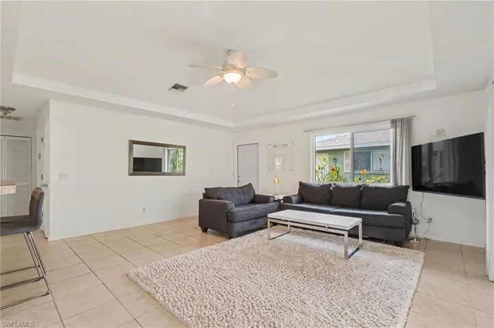 Living area with a raised ceiling, a ceiling fan, and light tile patterned flooring
