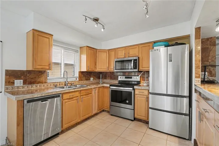 Kitchen with stainless steel appliances, light countertops, backsplash, and light tile patterned flooring