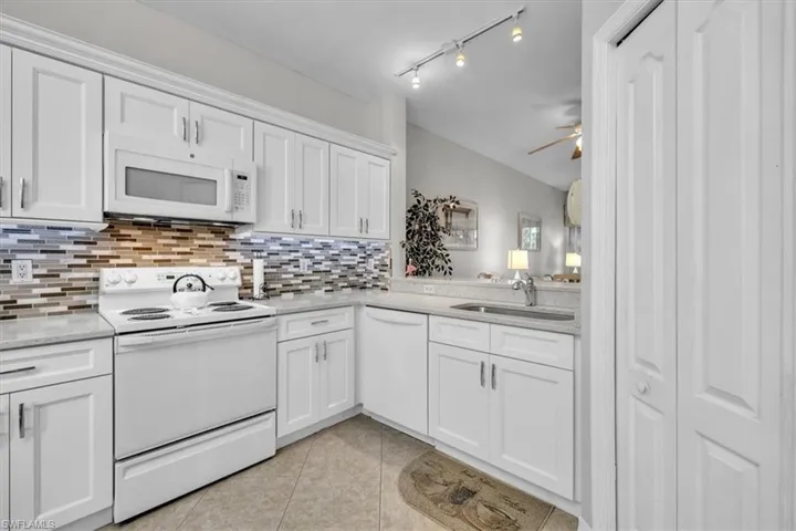 Kitchen with white appliances, white cabinetry, light tile patterned floors, light stone counters, and ceiling fan